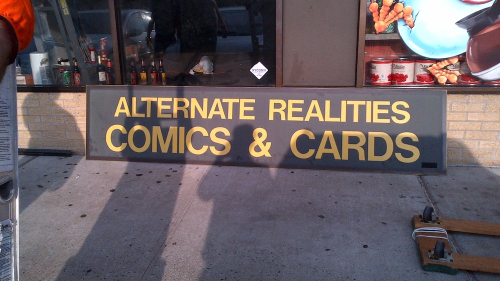 The sign for Alternate Realities Comics and Cards, sitting forlorn on the ground.